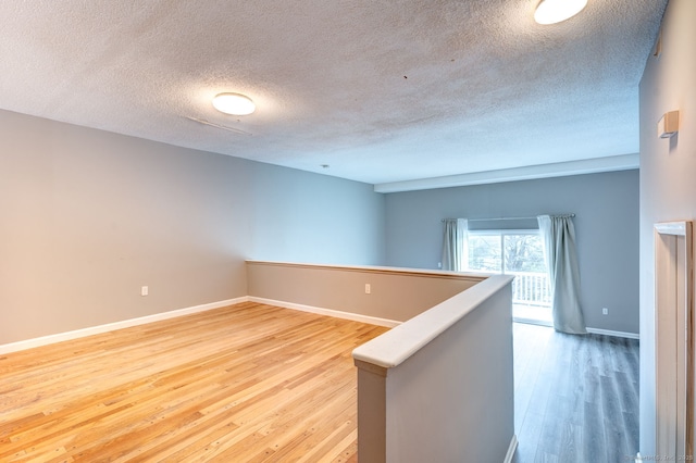 empty room featuring light wood-style flooring, a textured ceiling, and baseboards