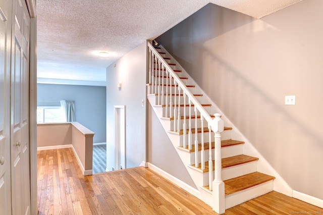 staircase featuring baseboards, wood-type flooring, and a textured ceiling