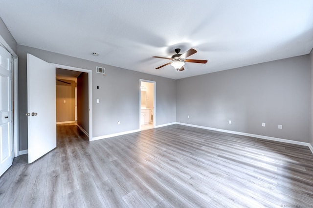 unfurnished bedroom with a ceiling fan, wood finished floors, visible vents, baseboards, and ensuite bathroom