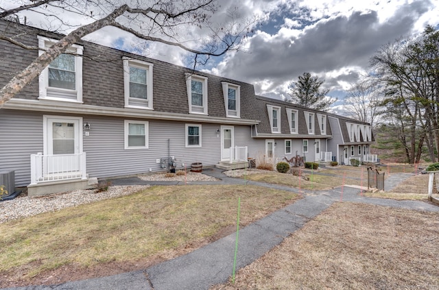 view of front of property with central AC unit, mansard roof, a front yard, and roof with shingles