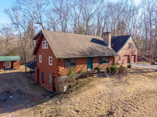 log home featuring an outbuilding, a detached garage, a shingled roof, log exterior, and a chimney