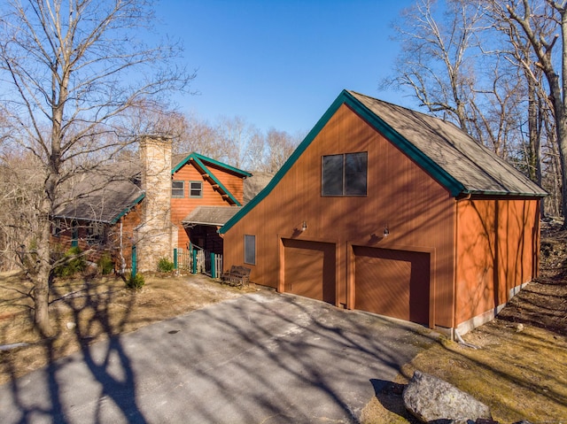 rustic home featuring a shingled roof, aphalt driveway, and a chimney