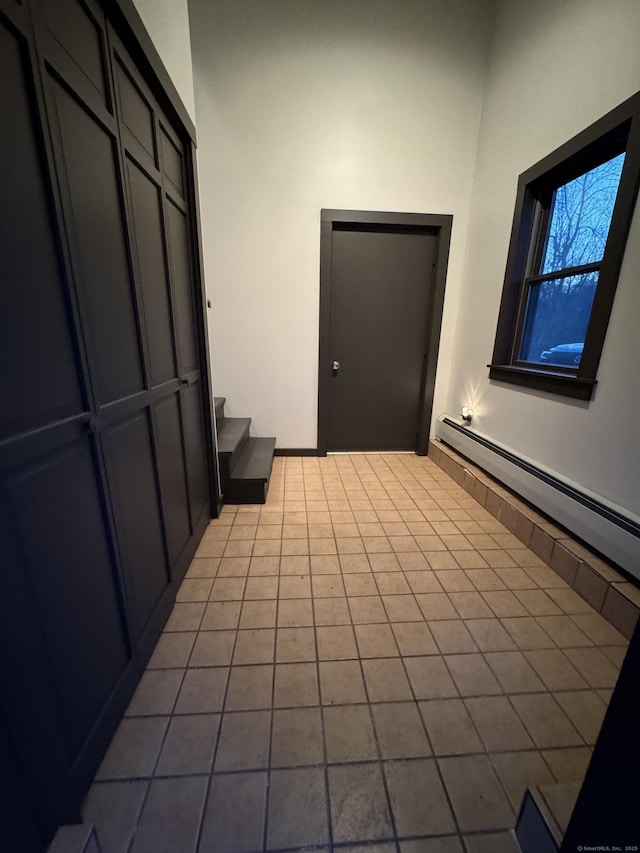 unfurnished room with tile patterned floors, a baseboard heating unit, and stairs