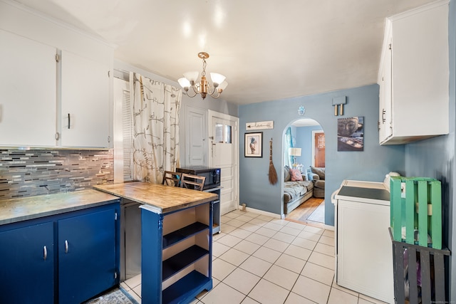 kitchen with backsplash, light tile patterned floors, arched walkways, white cabinetry, and blue cabinets