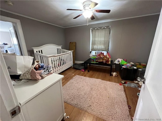 bedroom featuring crown molding, a nursery area, wood finished floors, and ceiling fan