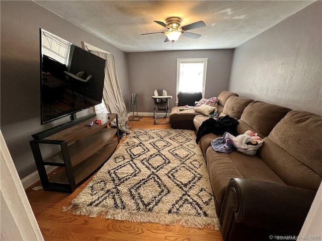 living area featuring wood finished floors, a ceiling fan, and baseboards