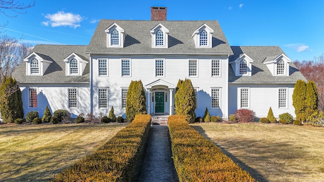 colonial house with a chimney, a front lawn, and a shingled roof