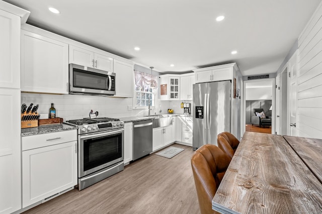 kitchen with light wood-style flooring, stone countertops, white cabinetry, stainless steel appliances, and decorative backsplash