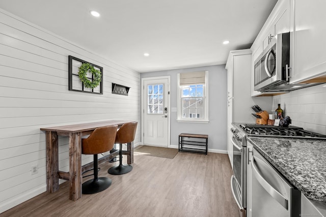 kitchen with dark stone countertops, stainless steel appliances, light wood finished floors, decorative backsplash, and baseboards