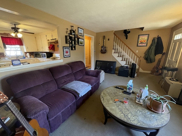 living room featuring stairway, baseboards, a ceiling fan, and carpet flooring