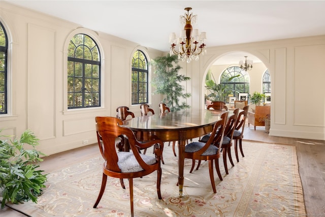 dining area with an inviting chandelier, a decorative wall, arched walkways, and light wood finished floors