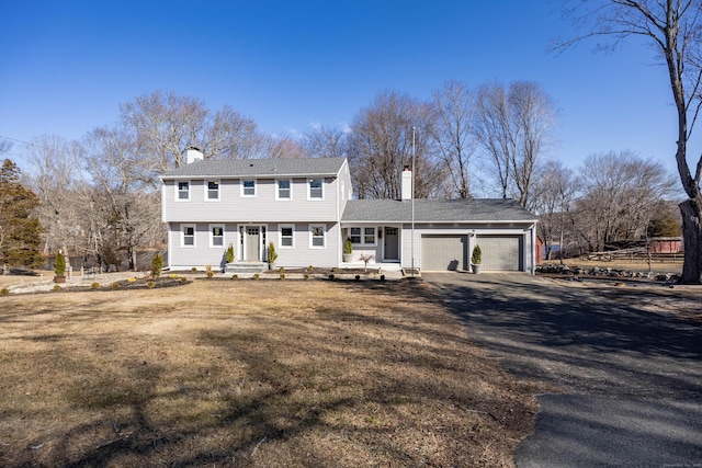 colonial-style house with a front yard, a garage, dirt driveway, and a chimney