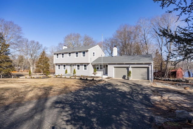 colonial home with driveway, a chimney, and an attached garage