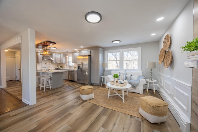 living room with recessed lighting, a wainscoted wall, wood finished floors, and a decorative wall