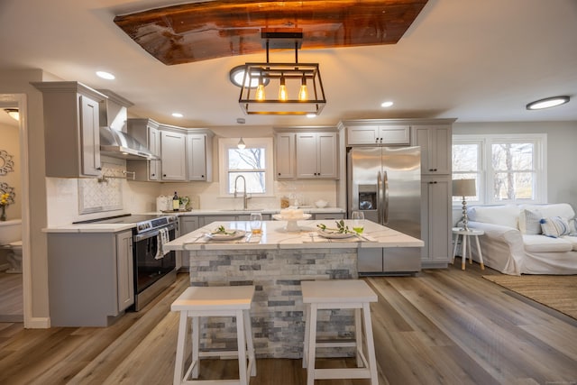 kitchen with a breakfast bar, gray cabinetry, decorative backsplash, stainless steel appliances, and wall chimney range hood