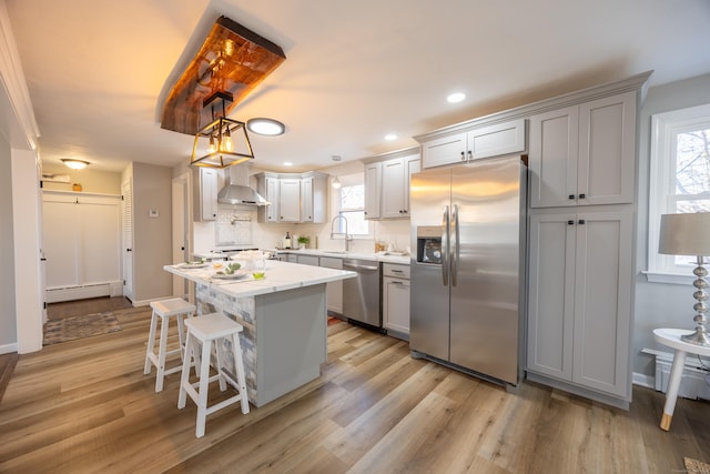 kitchen with a baseboard radiator, light wood-style flooring, appliances with stainless steel finishes, wall chimney range hood, and a center island