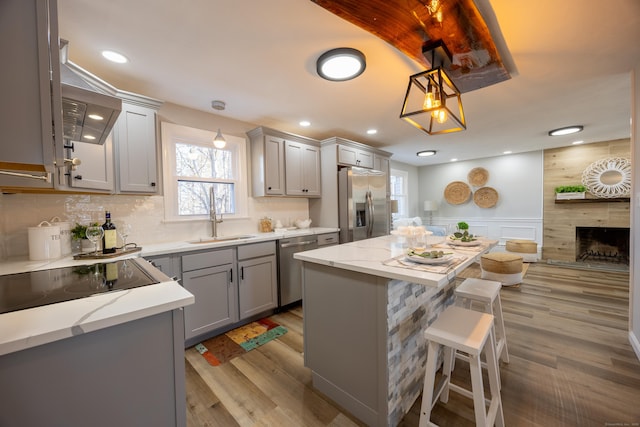 kitchen with gray cabinets, a sink, wood finished floors, appliances with stainless steel finishes, and a fireplace