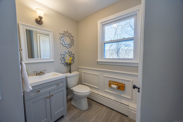 bathroom featuring a decorative wall, baseboard heating, vanity, and toilet