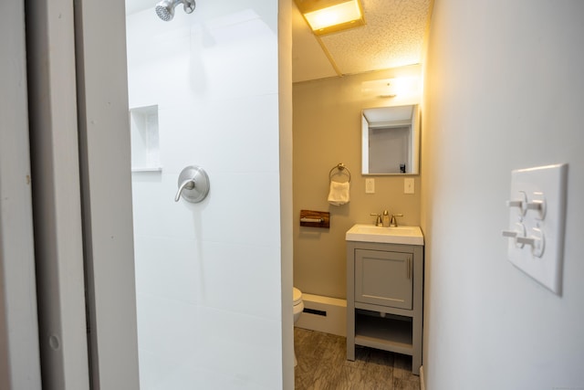 bathroom featuring toilet, a textured ceiling, wood finished floors, a shower, and vanity