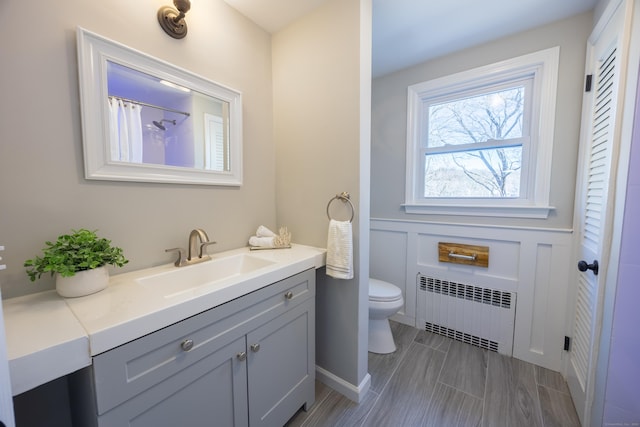 full bathroom featuring vanity, toilet, radiator heating unit, and a decorative wall