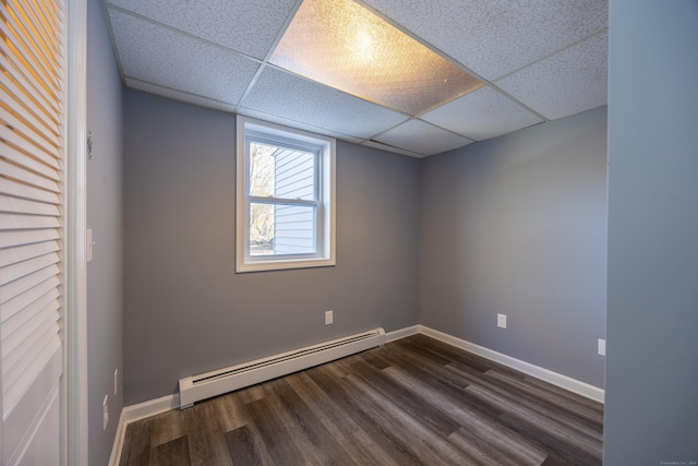 empty room with a baseboard heating unit, dark wood finished floors, baseboards, and a paneled ceiling