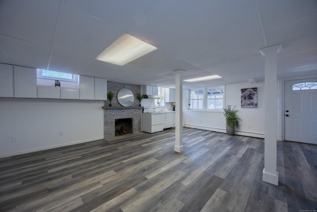 below grade area with dark wood-type flooring, a drop ceiling, washing machine and dryer, a fireplace, and a baseboard radiator