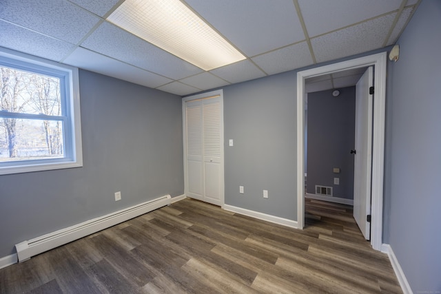 unfurnished bedroom featuring visible vents, baseboard heating, baseboards, dark wood-style floors, and a drop ceiling