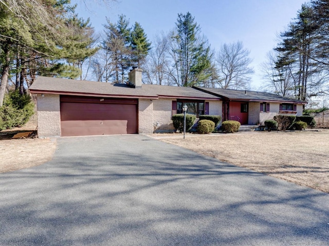 ranch-style home with aphalt driveway, an attached garage, brick siding, and a chimney