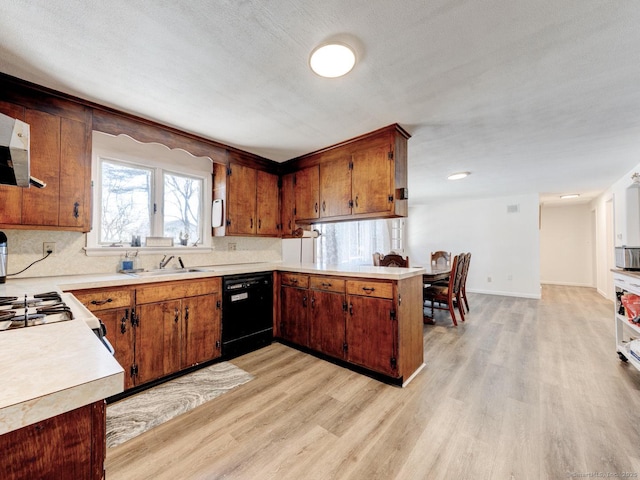 kitchen featuring dishwasher, light countertops, light wood-type flooring, a peninsula, and a sink