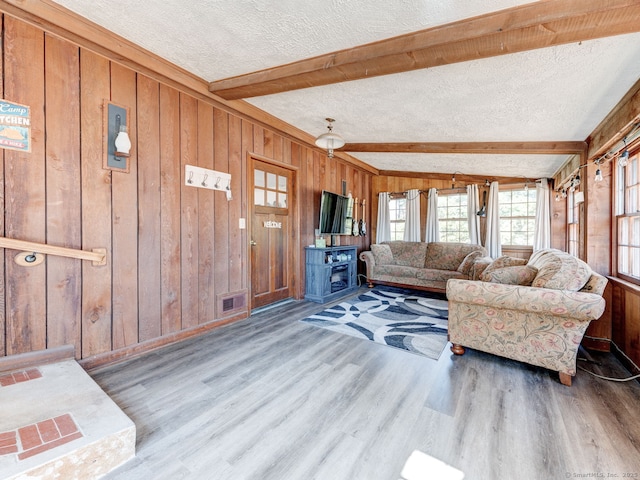 living room with visible vents, wooden walls, beamed ceiling, wood finished floors, and a textured ceiling