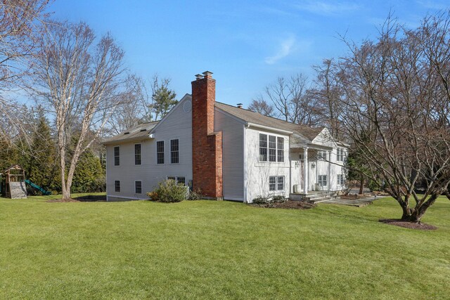 back of house featuring a playground, a chimney, and a yard