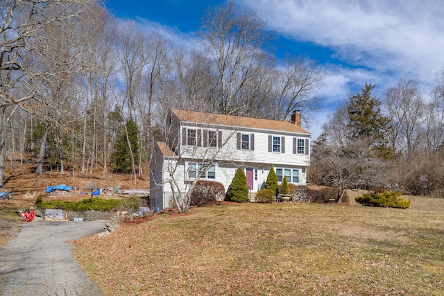 colonial home featuring driveway, a chimney, and a front yard