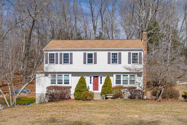 colonial house featuring entry steps, a front yard, and a chimney