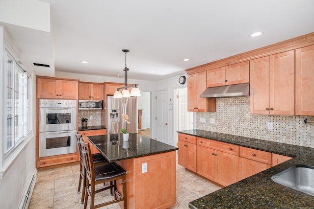 kitchen with backsplash, under cabinet range hood, baseboard heating, dark stone countertops, and appliances with stainless steel finishes