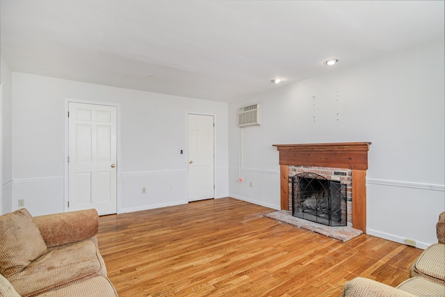 living area featuring a fireplace, baseboards, light wood-type flooring, and a wall unit AC