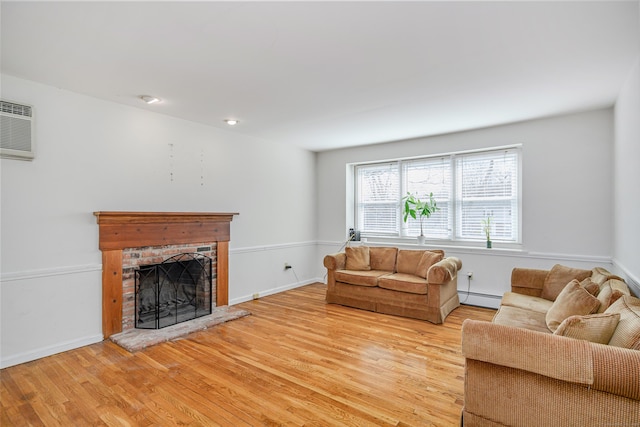 living area with baseboards, a wall unit AC, a fireplace, light wood-style floors, and a baseboard radiator