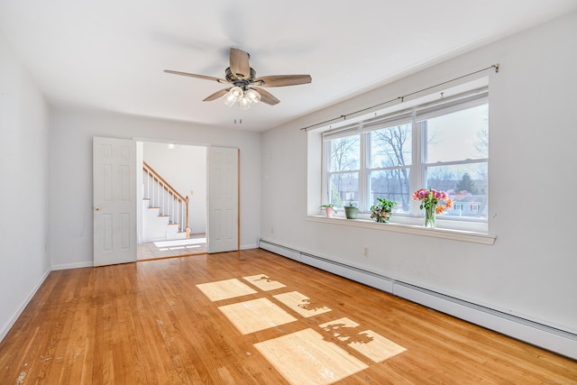 unfurnished room featuring baseboards, stairs, wood finished floors, a ceiling fan, and a baseboard radiator