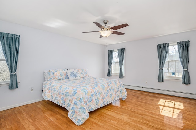 bedroom featuring a baseboard heating unit, multiple windows, wood finished floors, and baseboards