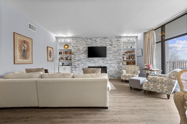 living room with a stone fireplace, built in features, wood finished floors, and visible vents