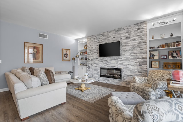 living room featuring visible vents, built in shelves, a large fireplace, baseboards, and wood finished floors