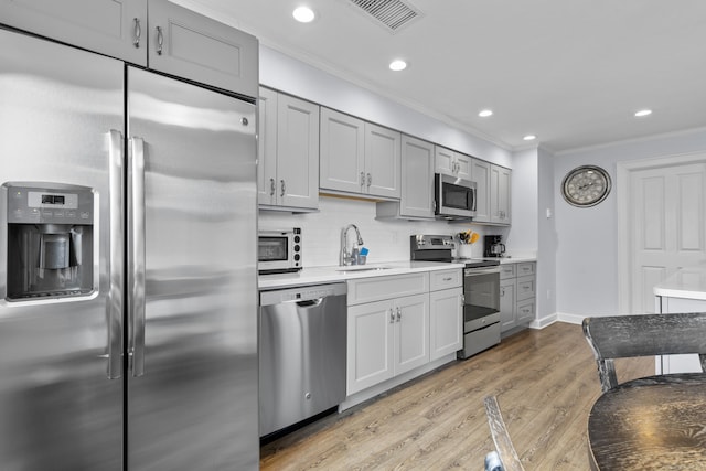 kitchen with visible vents, ornamental molding, light wood-style floors, appliances with stainless steel finishes, and backsplash