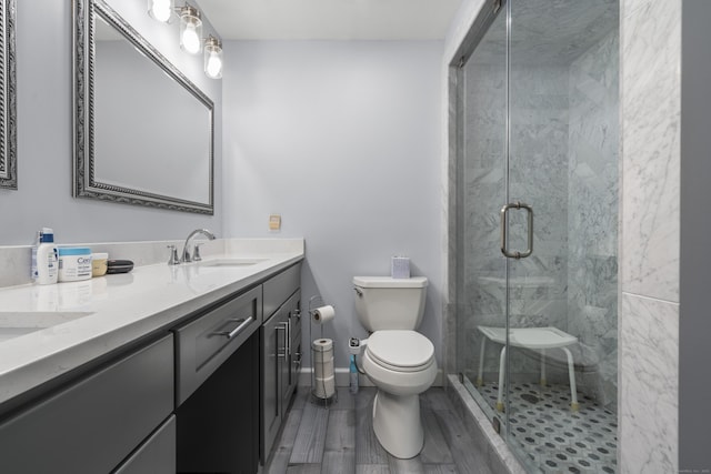 full bathroom with toilet, double vanity, a stall shower, wood finished floors, and a sink