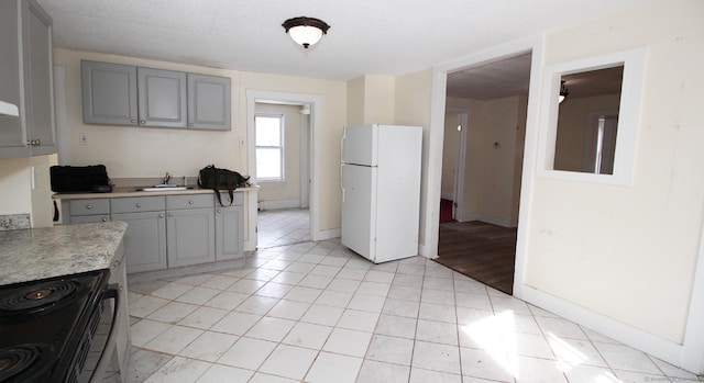 kitchen featuring light countertops, light tile patterned floors, gray cabinets, freestanding refrigerator, and electric range