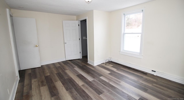 unfurnished bedroom featuring a baseboard heating unit, dark wood-style floors, baseboards, and a textured ceiling