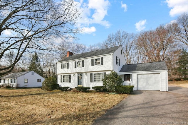 colonial house with a garage, driveway, a front lawn, and a chimney