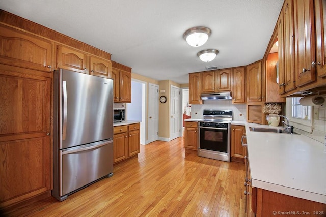 kitchen with light countertops, brown cabinetry, under cabinet range hood, and stainless steel appliances