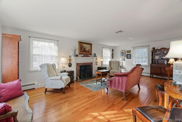 living area featuring a baseboard radiator, a brick fireplace, visible vents, and light wood finished floors