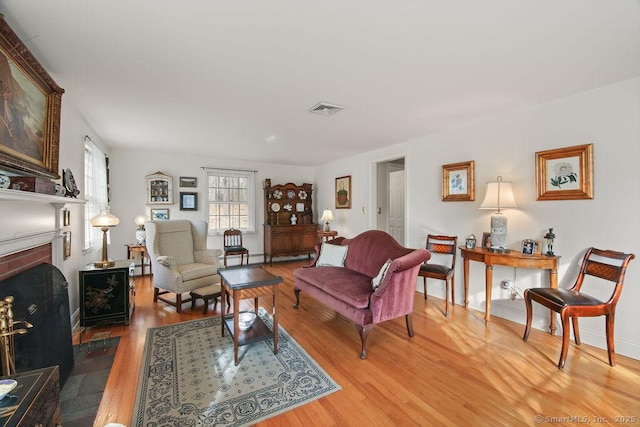 living room featuring a brick fireplace, light wood-style floors, and visible vents