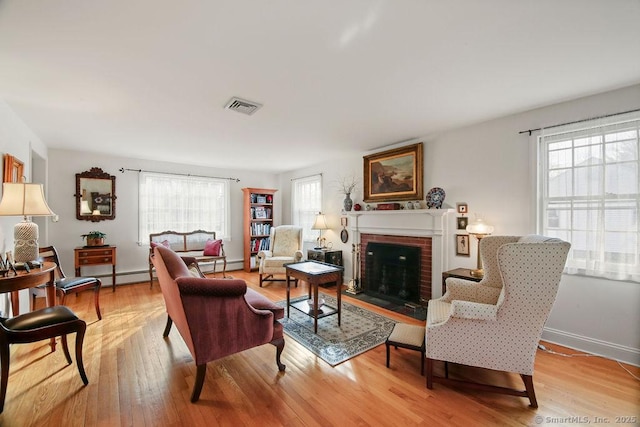 living room with visible vents, a brick fireplace, a healthy amount of sunlight, and light wood-style flooring