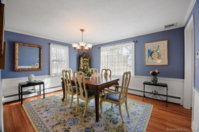 dining space featuring visible vents, a chandelier, ornamental molding, wood finished floors, and a baseboard radiator